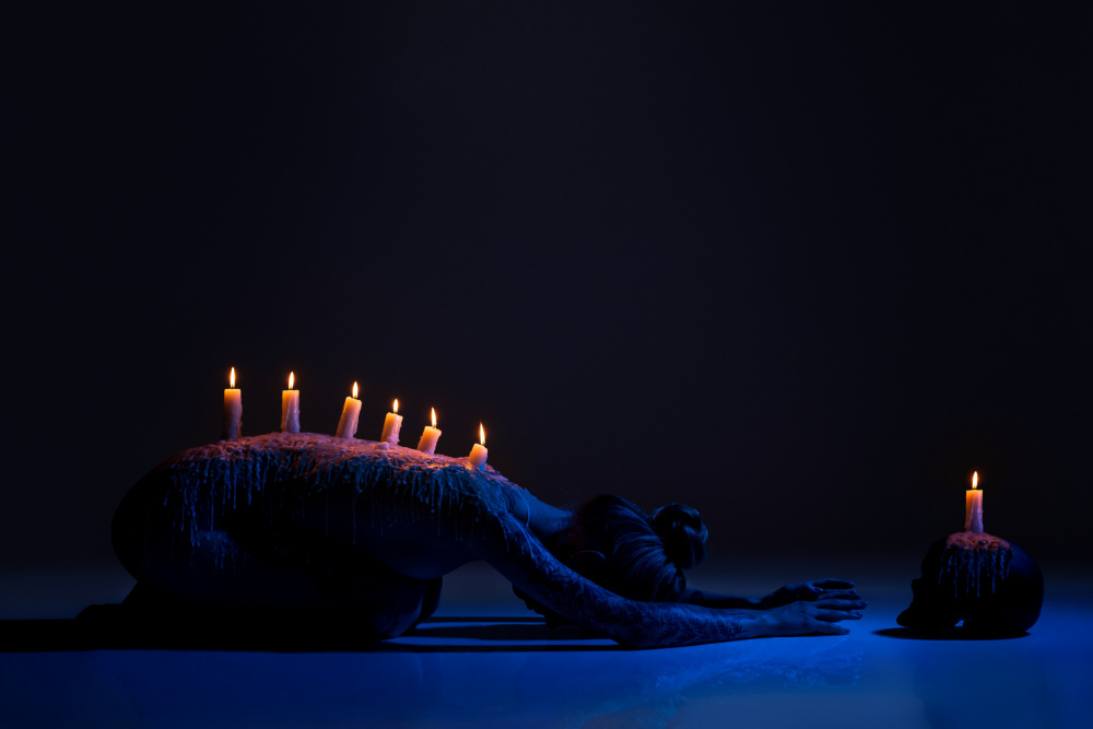 Burning candles on back of lady bowing down in darkness a Andrey Guryanov