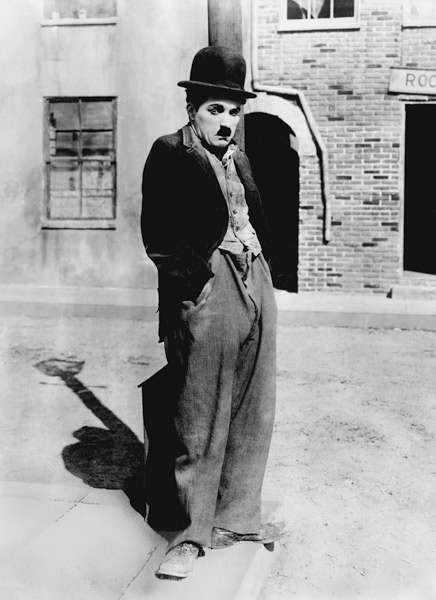 A dog 's life by and with Charlie Chaplin , standing in a street, hands in pockets. Los Angeles a English Photographer, (20th century)