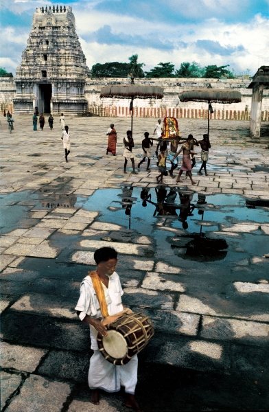 Drummer and devotees reflected in pool of water (photo)  a 