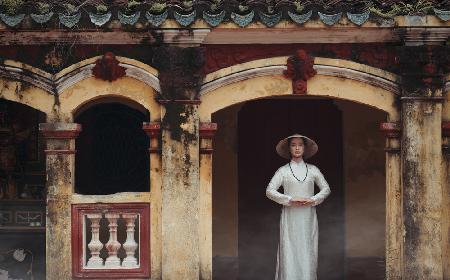 A Vietnamese girl in a traditional ao dai dress is praying for happiness